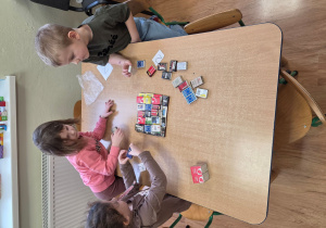 Franek, Mariana i Pola budują piramidę z pudełek od zapałek.