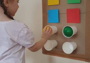 Dziewczynka układa piłki do kubków według wzoru.