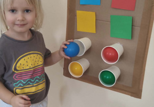 Dziewczynka układa piłki do kubków według wzoru.