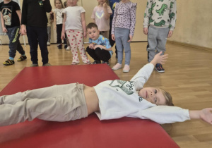 Dziewczynka leży na materacu i rozciąga się.