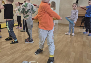 Chłopiec ćwiczy skręty tułowia z pomocą szarfy.