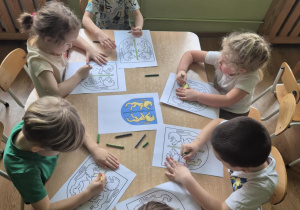 Sześcioro dzieci siedzi przy stoliku i koloruje herb Kutna.