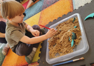 Chłopiec szuka szczątków dinozaura w piasku.