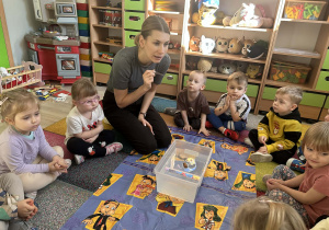 Dzieci siedzą na dywanie w kole i wspólnie obserwują co tonie a co pływa.