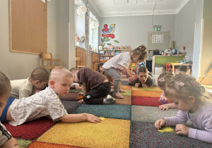 Dzieci leżą na dywanie i dmuchają na piórka.