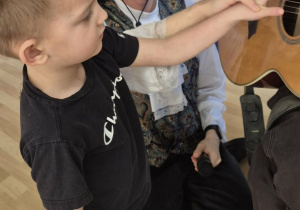 Chłopiec gra na gitarze trzymanej przez muzyka