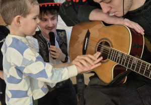 Chłopiec gra na gitarze trzymanej przez muzyka