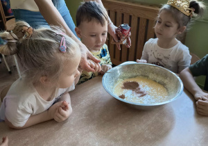 Chłopiec przy pomocy nauczycielki dodaje do ciasta przyprawy