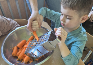 Chłopiec z pomocą nauczycielki ściera marchewkę