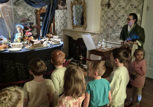 Dzieci przy zastawionym historycznymi potrawami stole słuchają opowieści przewodniczki