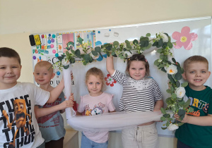 Zdjęcie dziewczynek w kwiatowej ramce trzymanej przez chłopców z grupy.
