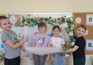 Zdjęcie dziewczynek w kwiatowej ramce trzymanej przez chłopców z grupy.