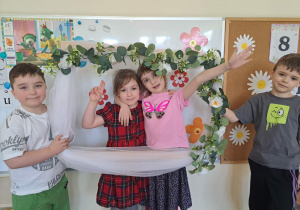 Zdjęcie dziewczynek w kwiatowej ramce trzymanej przez chłopców z grupy.