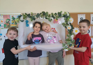 Zdjęcie dziewczynek w kwiatowej ramce trzymanej przez chłopców z grupy.