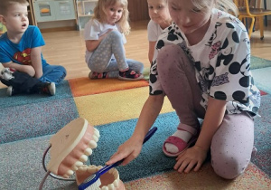 Dziewczynka prezentuje jak myć zęby.