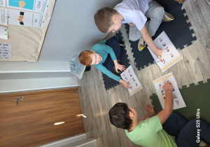 Chłopcy wskazują i zaznaczają kredką w odpowiednim kolorze na obrazku dzieci smutne i wesołe