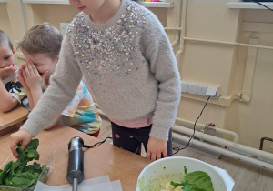 Dzieci dodają szpinak do miski z owocami.