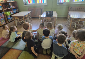 Dzieci siedzą na dywanie, oglądają film