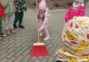 Dziewczynka zamiata kostkę przy przedszkolnym ogrodzie