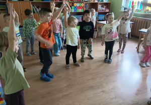 Dzieci w sali przedszkolnej wykonują ćwiczenia na obręcz barkową