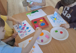 Dzieci stemplują kulką z kartki umoczoną w farbie.