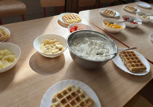 Na stole zostały przygotowane gofry, bita śmietana i owoce do dekarocja