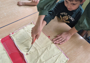 Chłopiec z pomocą nauczycielki kroi ciasto