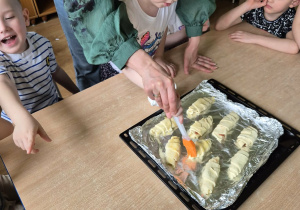 Dziewczynka z pomocą nauczycielki smaruje rogaliki roztrzepanym jajkiem