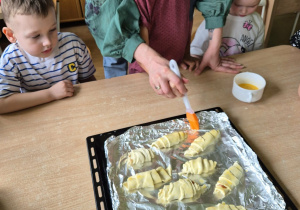 Chłopiec z pomocą nauczycielki smaruje rogaliki roztrzepanym jajkiem