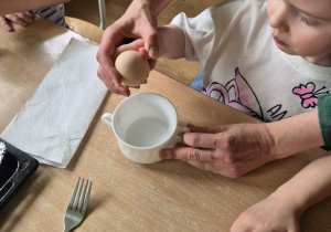 Dziewczynka z pomocą nauczycielki rozbija jajko