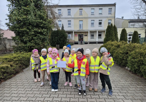 Dzieci stoją przed SP nr 4, dwoje z nich trzyma w rękach kopertę z kartką świąteczną