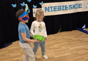 Dziewczynka prowadzi chłopca, który ma zawiązane oczy