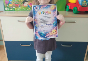 dziewczynka pozuje do zdjęcia z dyplomem