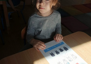 dziewczynka pozuje do zdjęcia z wykonaną kartą pracy