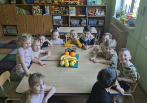 Dzieci siedzą przy stolikach, przed nimi leżą owoce