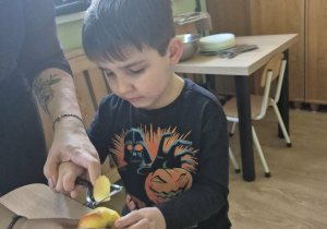 Chłopiec z pomocą nauczycielki obiera jabłko