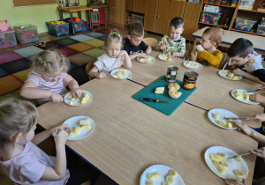 Siedzące przy stolikach dzieci kroją owoce