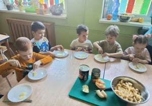 Siedzące przy stolikach dzieci kroją owoce