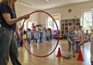 Dziewczynka przerzuca woreczek przez obręcz trzymaną przez nauczycielkę