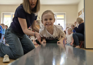 Dziewczynka w asyście nauczycielki wykonuje ćwiczenie na ławce