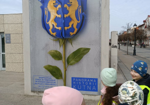Dzieci biorą udział w spacerze ulicami miasta, obserwując najważniejsze budynki.