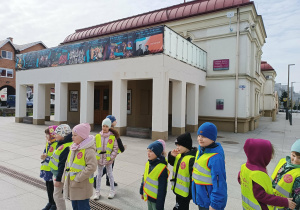 Dzieci biorą udział w spacerze ulicami miasta, obserwując najważniejsze budynki.