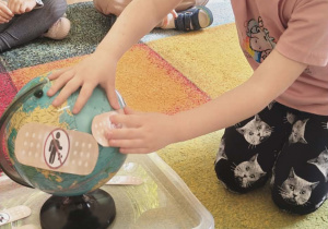 Dziewczynka przykleja plaster na globus.