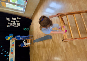 Dzieci w trakcie wykonywania konkurencji: przejście po drabince i przeskok przez ławeczkę gimnastyczną.