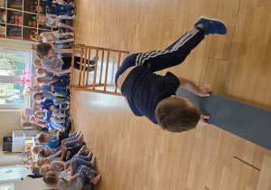 Dzieci w trakcie wykonywania konkurencji: przejście po drabince i przeskok przez ławeczkę gimnastyczną