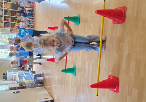 Dzieci w trakcie wykonywani konkurencji: przeskok obunóż przez laski gimnastyczne na różnych wysokościach.