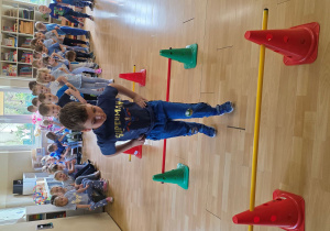 Dzieci w trakcie wykonywani konkurencji: przeskok obunóż przez laski gimnastyczne na różnych wysokościach