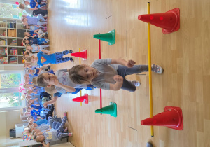 Dzieci w trakcie wykonywani konkurencji: przeskok obunóż przez laski gimnastyczne na różnych wysokościach