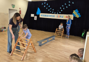 Dzieci w trakcie wykonywania konkurencji: przejście po drabince i przeskok po ławeczce.