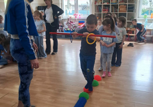 Dzieci w trakcie konkurencji: przejście po ścieżce sensorycznej z laska gimnastyczną.
